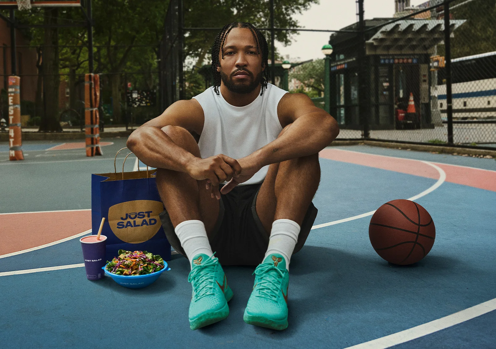 Jalen Brunson on a basketball court with a Just Salad bowl, smoothie, and bag beside him.
